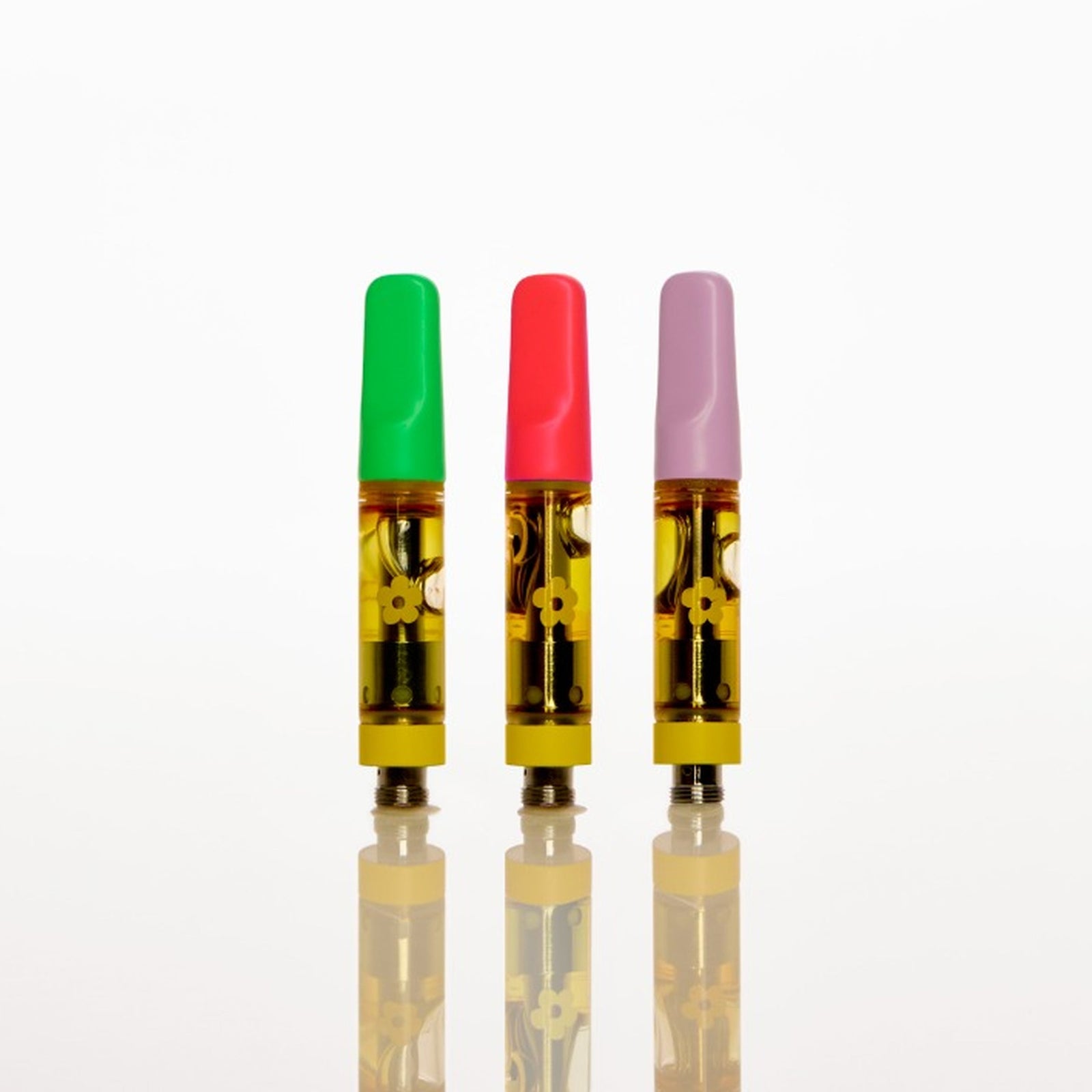 Three small vape cartridges with translucent yellow bodies and colored tops in green, red, and purple, standing upright on a reflective white surface against a white background.